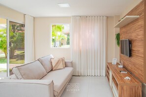 Una sala moderna con un sofá, cortinas, un televisor y un mueble de madera.