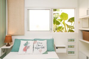 A bedroom with a bed, a window, a bedside table with a lamp, and a wall with storage units. - Solar Água Pipa- Summer Pipa (Tibau do Sul)