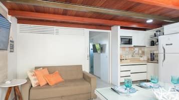 A compact living space with a kitchenette, a sofa with decorative pillows, and a dining area with a glass table set for two.