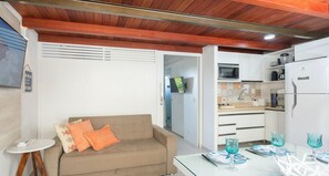 En kompakt opholdsstue med et tekøkken, en sofa med dekorative puder og et spiseområde med et glasbord dækket til to personer.