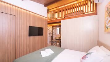 A hotel room with a bed, a flat-screen TV mounted on the wall, a wooden ceiling, and a balcony with a railing.