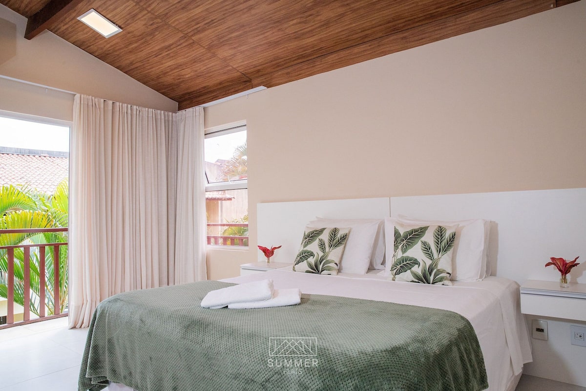 Un dormitorio con techo de madera, una cama con manta verde, almohadas blancas y una mesita de noche con un florero.