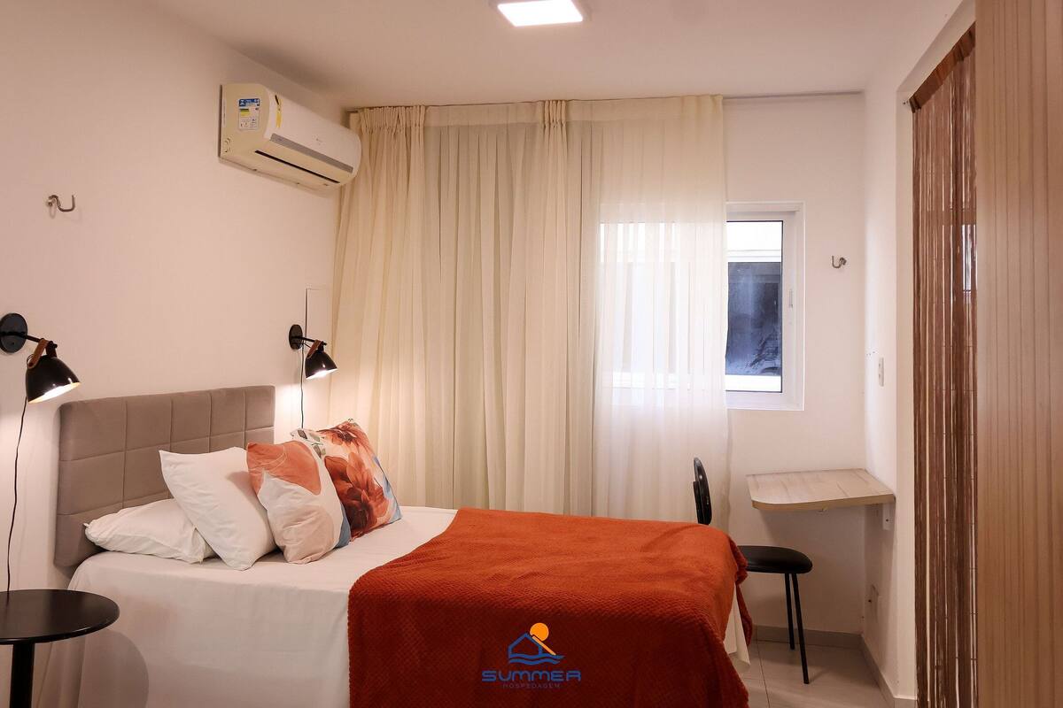 Una habitación de hotel con cama, escritorio, aire acondicionado y ventana con cortinas.