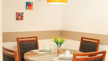 Uma mesa de jantar redonda com cadeiras, um vaso com flores, um jarro branco e um copo sobre a mesa.