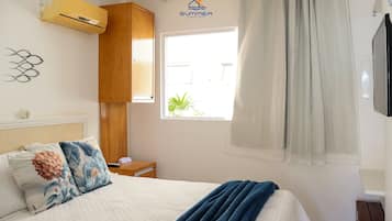 Ein Schlafzimmer mit Bett, einem fensterbelaubten Fenster, einer Klimaanlage und einem an der Wand montierten Fernseher.