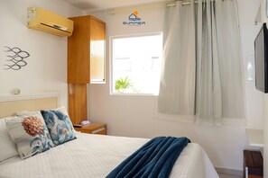 A bedroom with a bed, a window with curtains, an air conditioning unit, and a wall-mounted TV.