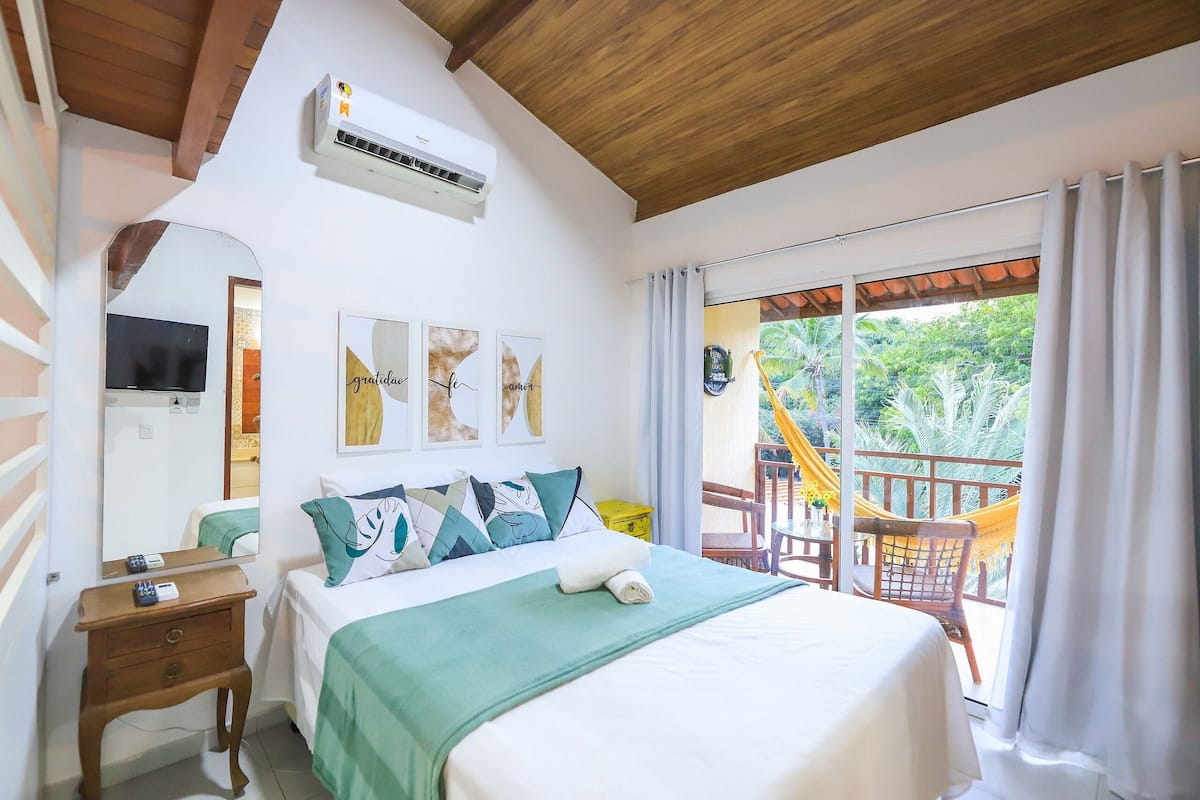 Habitación de hotel con cama, mesita de noche, televisor y balcón con una silla y una hamaca.