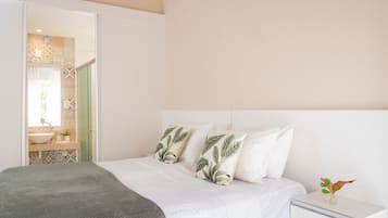 Un dormitorio con cama, almohadas, una mesita de noche y una planta pequeña.