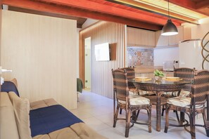 Un comedor con sillas de mimbre y una mesa de vidrio, una cocina con refrigerador y salpicadero de azulejos, y un techo de madera.
