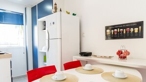 A compact kitchen with a refrigerator, a dining table with placemats, and a wall-mounted beer chart. - Solar Água Pipa- Summer Pipa (Tibau do Sul)