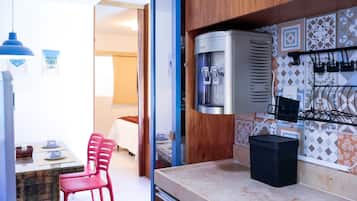 Een kitchenette met een waterdispenser, een zwarte prullenbak en een betegelde spatwand.