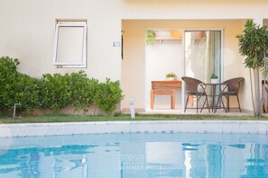 A swimming pool with a tiled edge, a small table with chairs, and a potted plant.