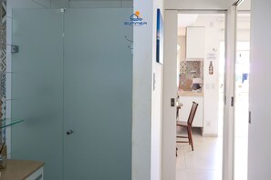 A hotel room with a glass door, a dining area with a table and chairs, and a kitchen visible through an open door. - Solar Água Pipa- Summer Pipa (Tibau do Sul)