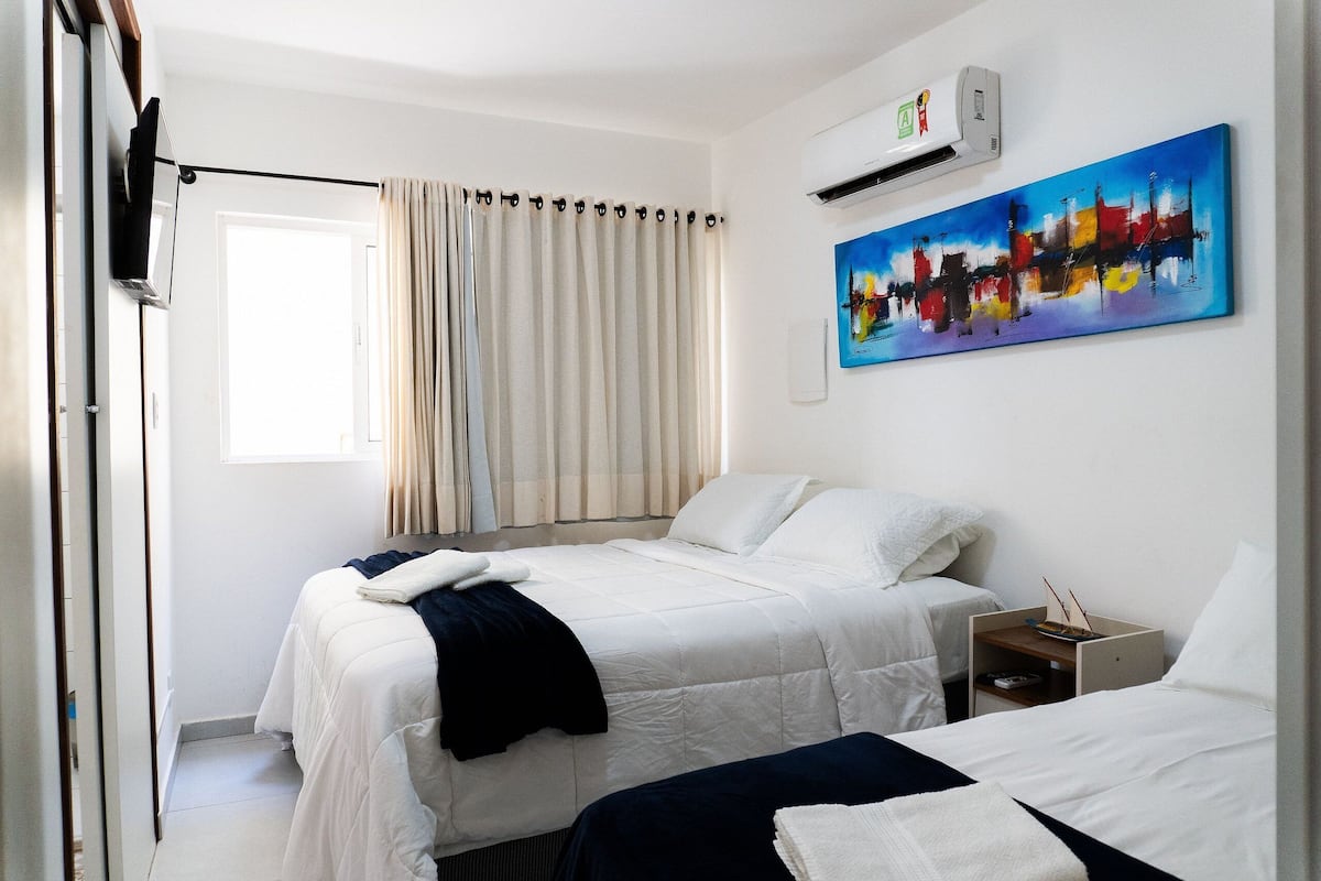 Habitación de hotel con dos camas, un cuadro, aire acondicionado y una ventana con cortinas.