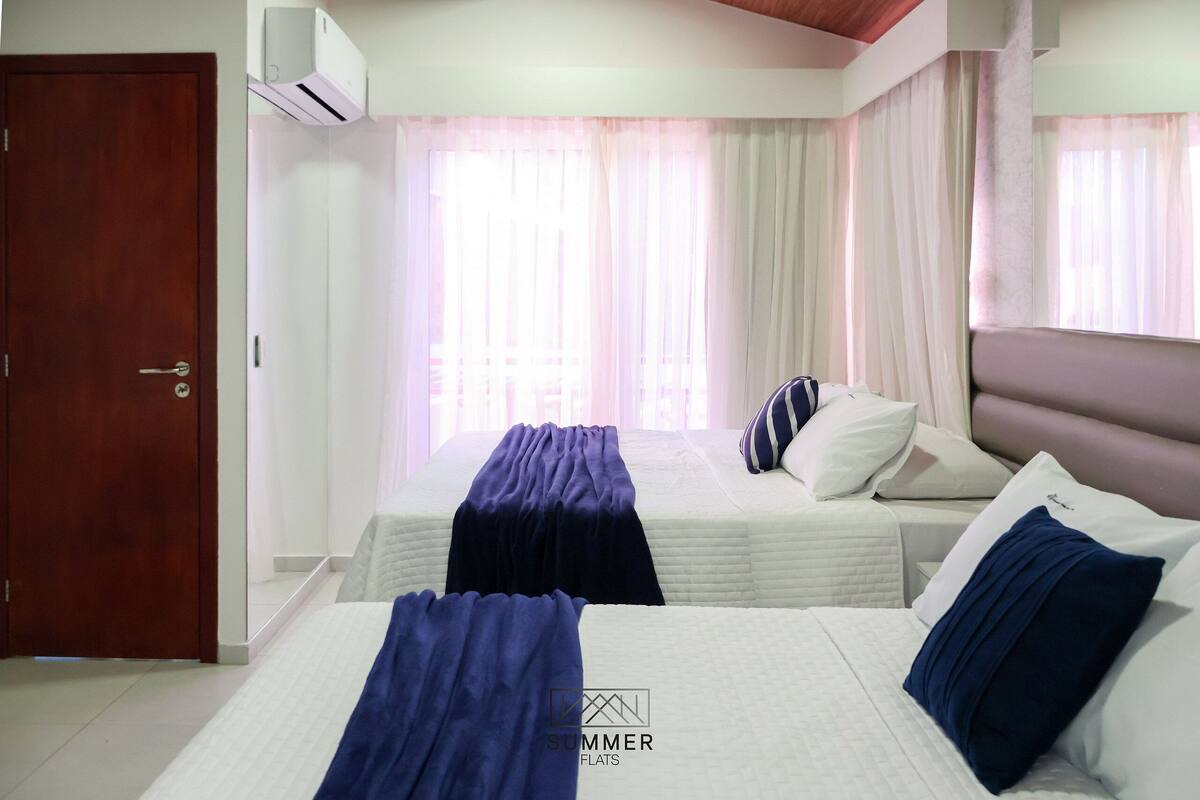 Una habitación de hotel con dos camas, una puerta de madera y una ventana con cortinas traslúcidas.
