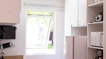 Cozinha compacta com janela, armários brancos, micro-ondas embutido e máquina de café.