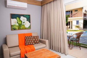 A living room with a sofa, a painting, a window with curtains, and a view of an outdoor balcony.
