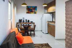 A compact living space with a sofa, dining table, chairs, kitchen area, and a refrigerator.