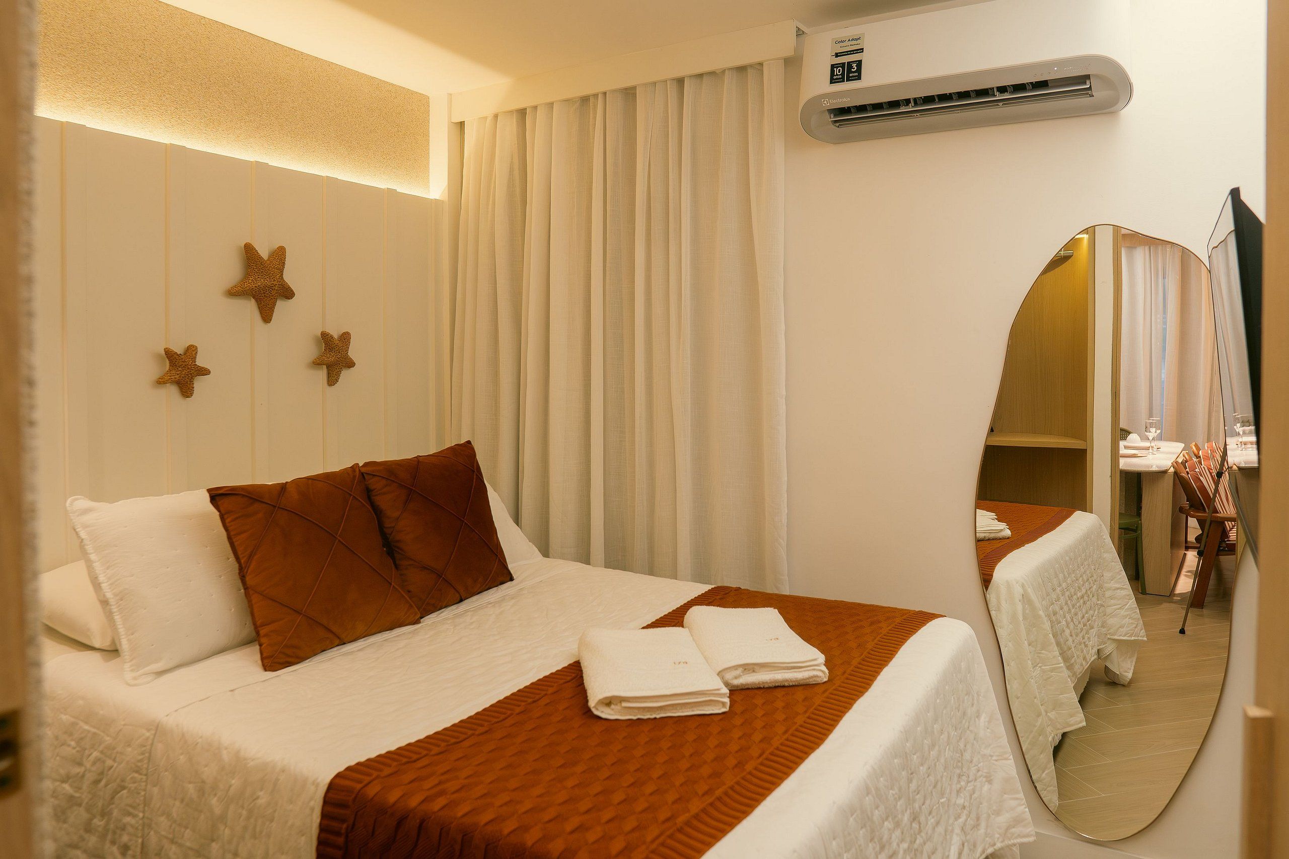 Una camera d'albergo con un letto, uno specchio, una finestra con tende e un condizionatore d'aria.
