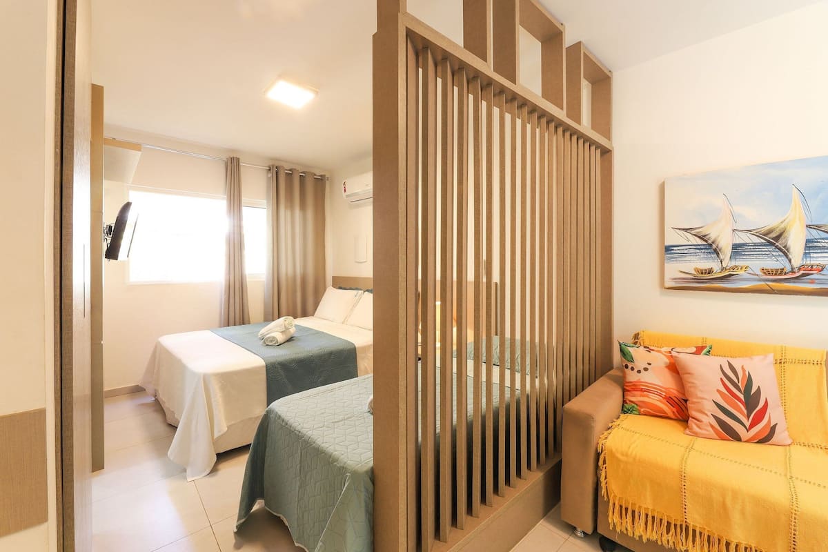 Habitación de hotel con dos camas, un sofá, un cuadro y una ventana con cortinas.