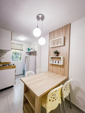 A compact kitchen with a dining table, chairs, a refrigerator, and a window. - Solar Água Pipa- Summer Pipa (Tibau do Sul)