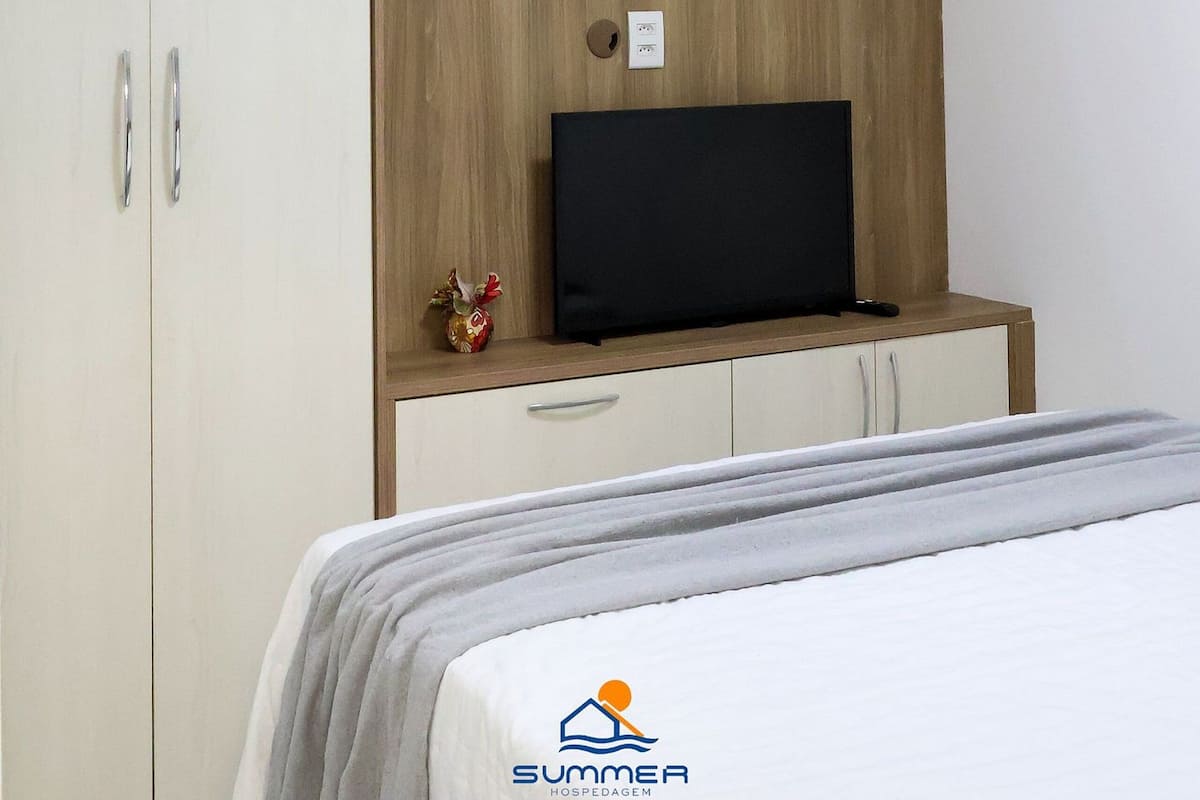 Un dormitorio con cama, armario, televisor y estante con fotografías.