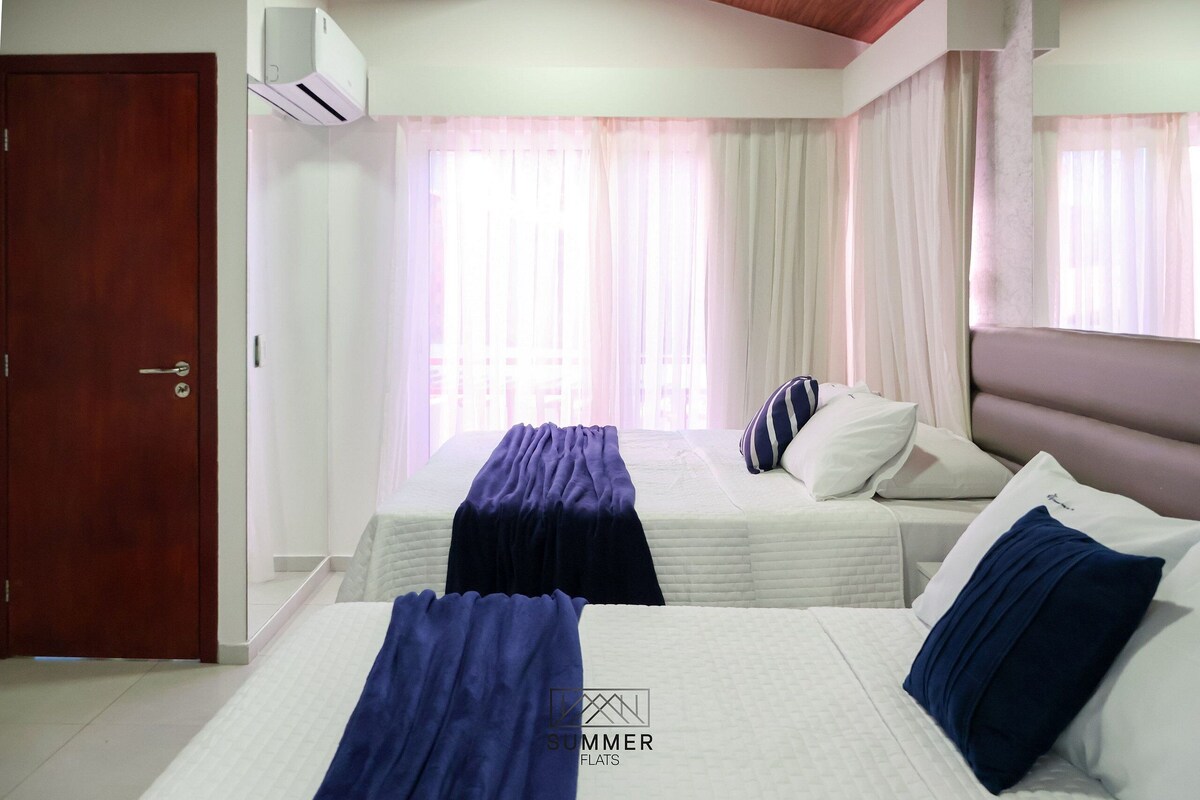 A hotel room with two beds, a wooden door, and a window with sheer curtains.