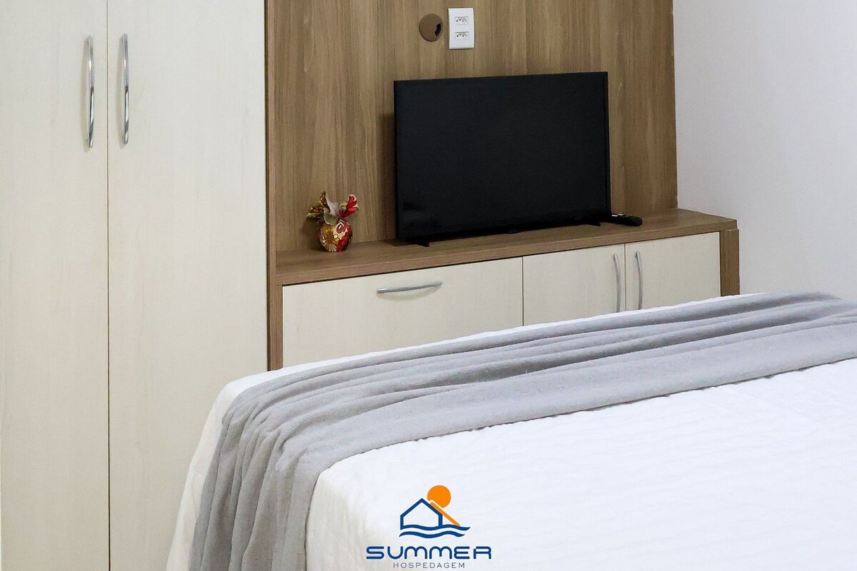 A bedroom with a bed, a wardrobe, a TV, and a shelf with pictures.