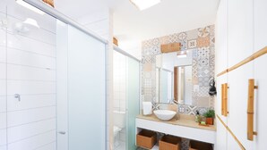A bathroom with a glass shower door, a white sink with a vessel basin, a patterned backsplash, and wicker baskets under the sink. - Solar Água Pipa- Summer Pipa (Tibau do Sul)