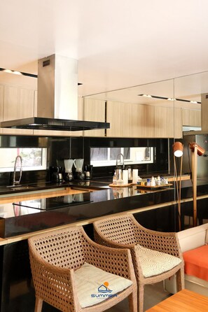 A modern kitchen with a black countertop, stainless steel appliances, and wicker chairs. - Solar Água Pipa- Summer Pipa (Tibau do Sul)