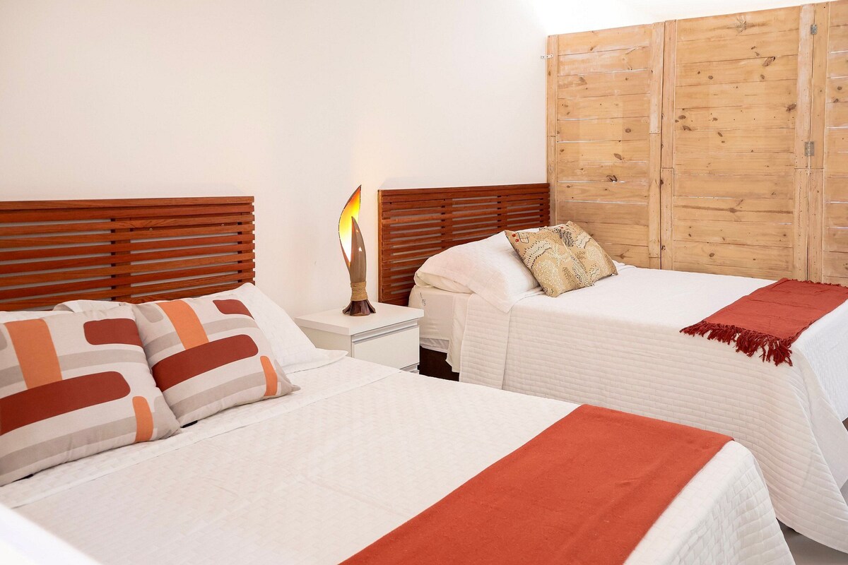 A hotel room with two beds, wooden headboards, a nightstand, and a bedside lamp.