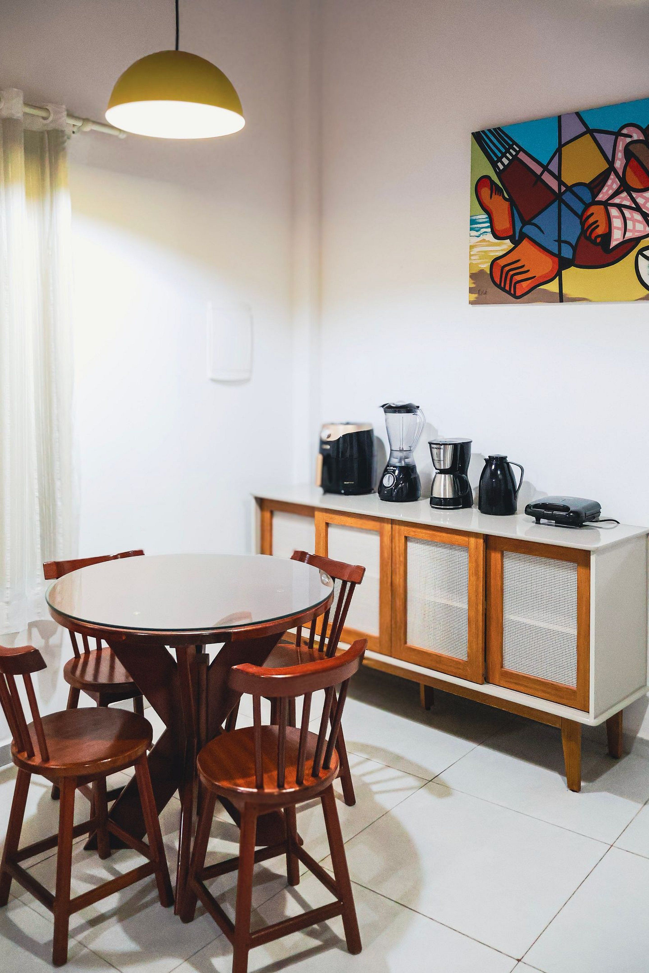 Un comedor con una mesa redonda, sillas de madera, un mueble con electrodomésticos y un cuadro en la pared.