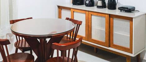 Un comedor con una mesa redonda, sillas de madera, un mueble con electrodomésticos y un cuadro en la pared.