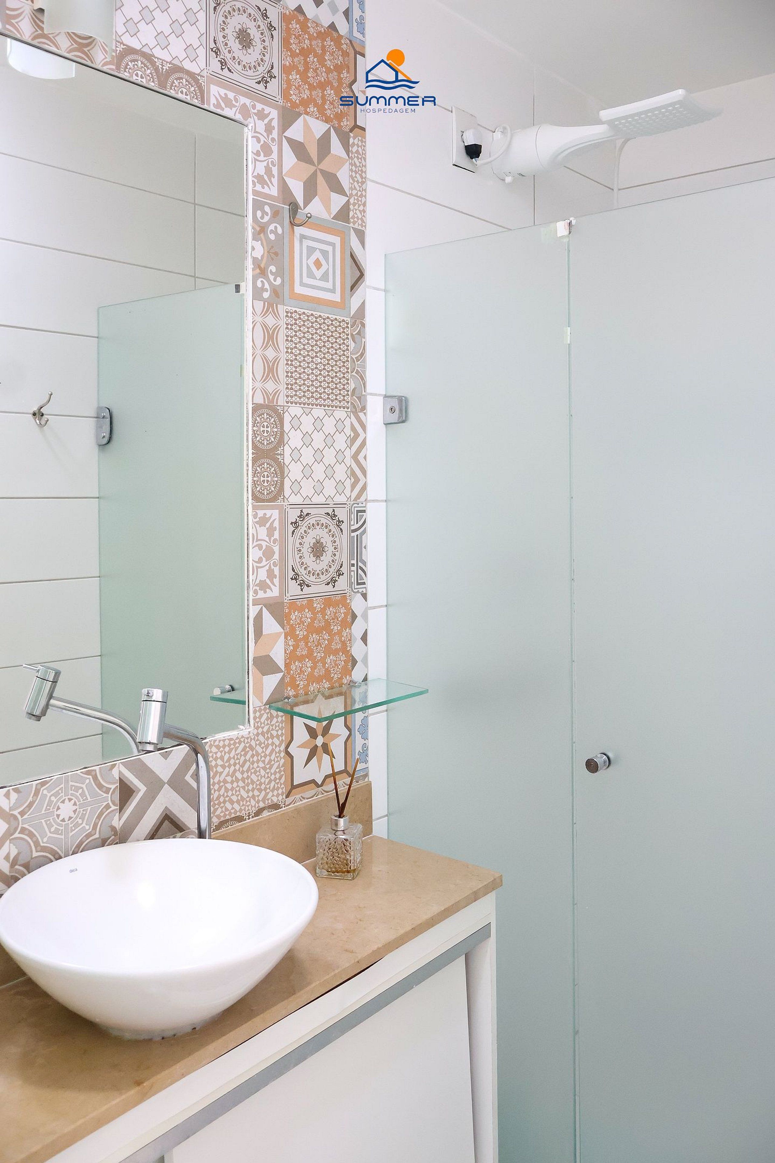 A bathroom with a white sink, a glass shower enclosure, and a patterned tile backsplash.