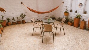 A patio with a round table and four wicker chairs, surrounded by potted plants and a hammock. - Toukan Hostel (Pereira)