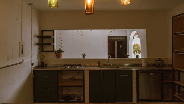 A kitchen with dark cabinets, a stove, a sink, and hanging pendant lights. - Toukan Hostel (Pereira)