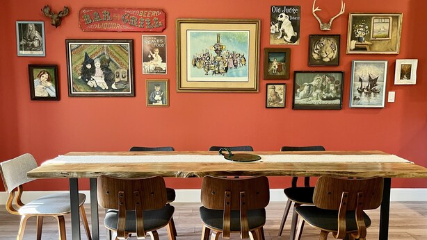 Een eetgedeelte met een lange houten tafel en moderne stoelen, omringd door diverse lijstwerken aan de muren.