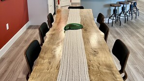 Een ruime eethoek met een lange houten tafel, omringd door stoelen, en een keuken met witte kasten en roestvrijstalen apparatuur.