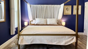 Een hemelbed met een baldakijn, wit beddengoed en een houten vloer.