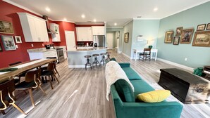 Een moderne keuken met witte kastjes, een centraal eiland met krukken, en een eetgedeelte met een houten tafel en stoelen.