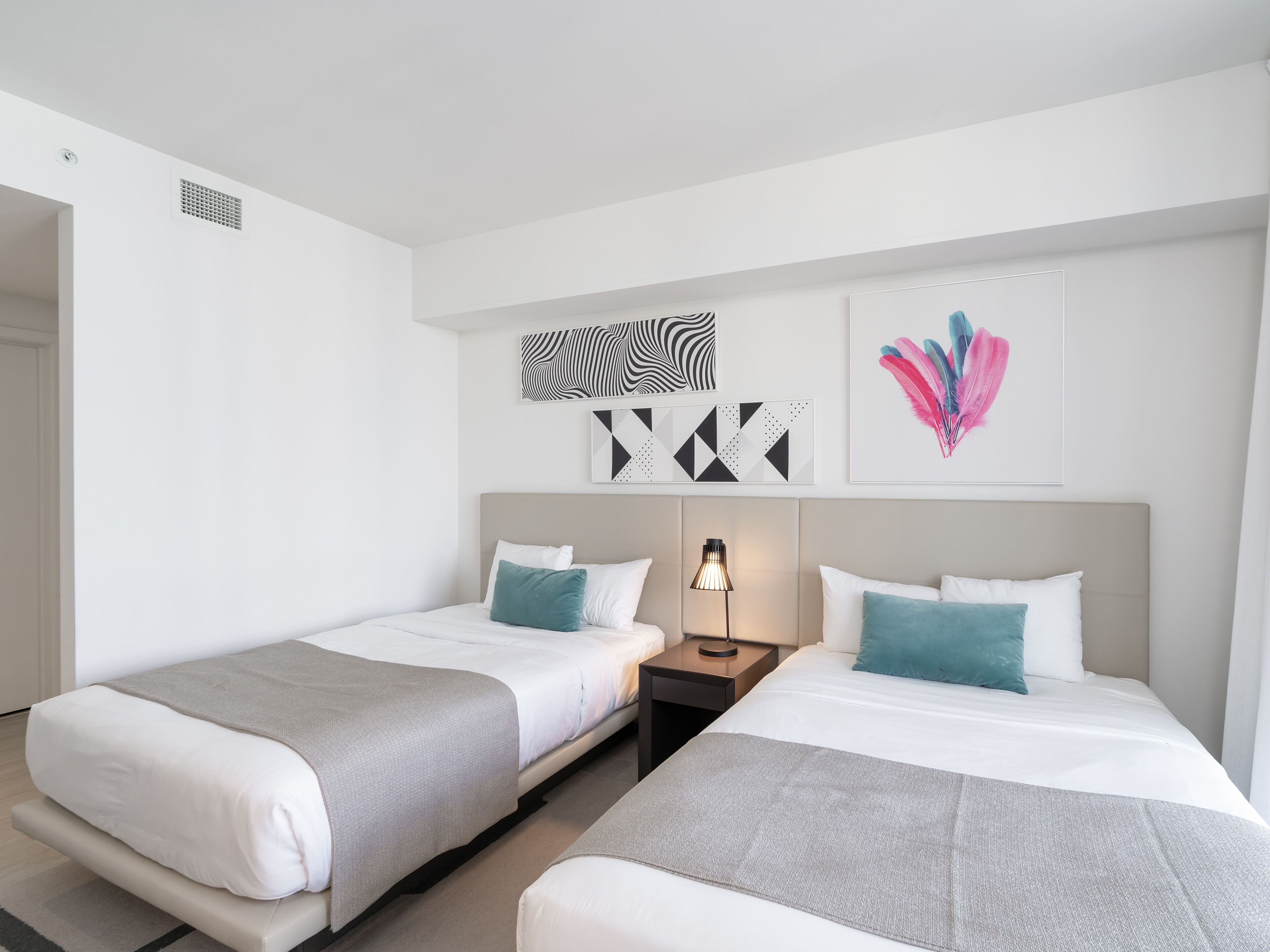 A hotel room with two beds, a nightstand, a lamp, and wall art.
