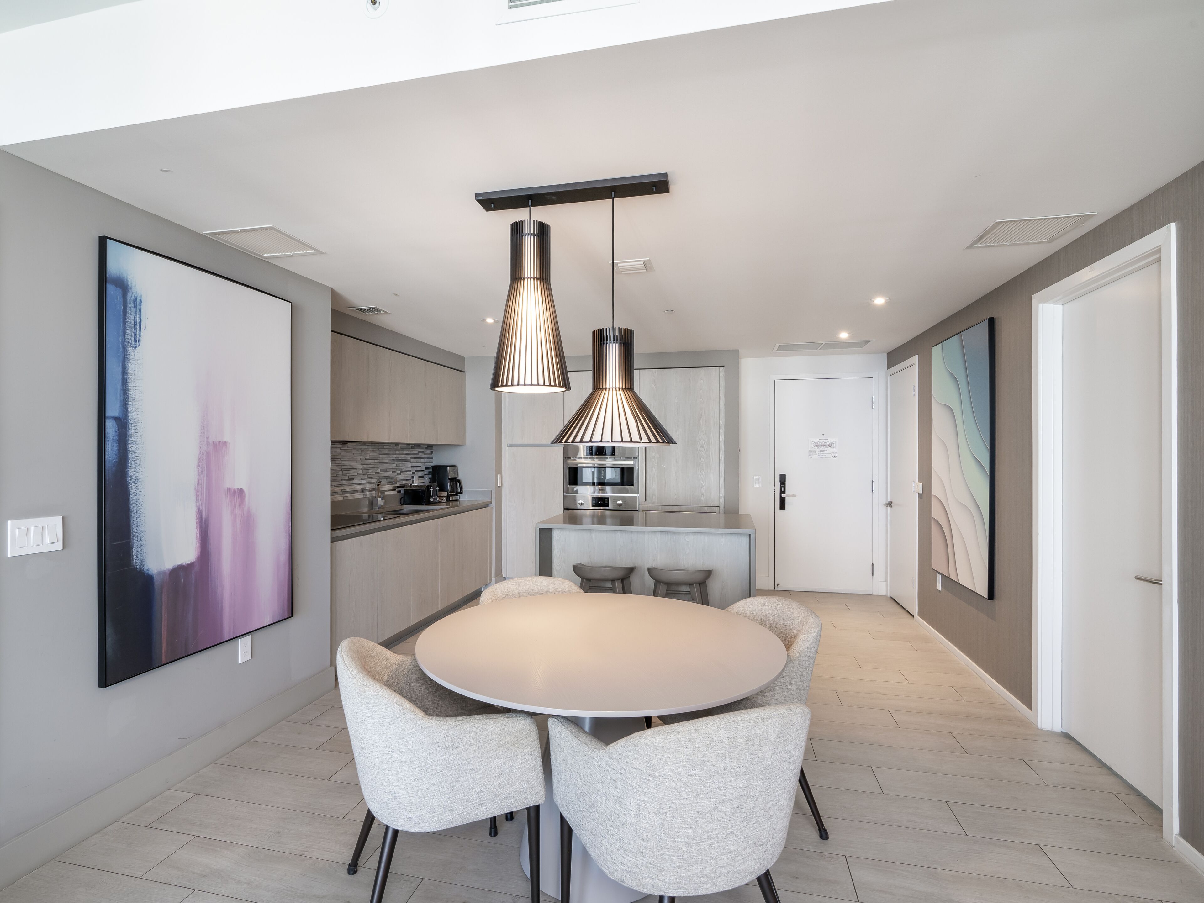 Una cocina moderna con una isla central, iluminación colgante y un comedor con una mesa redonda y cuatro sillas.