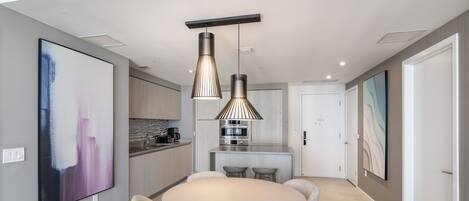 Una cocina moderna con una isla central, iluminación colgante y un comedor con una mesa redonda y cuatro sillas.