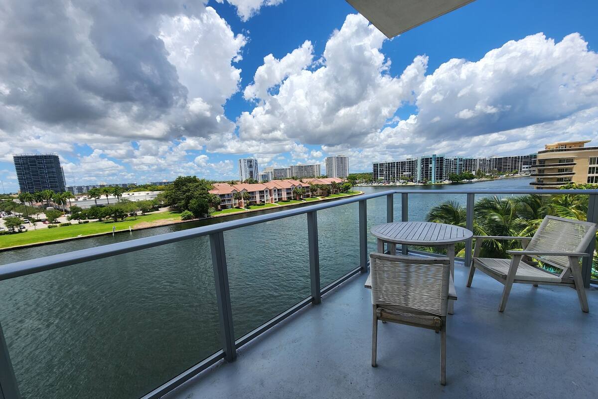 A balcony with a view of a river, a table, and two chairs.