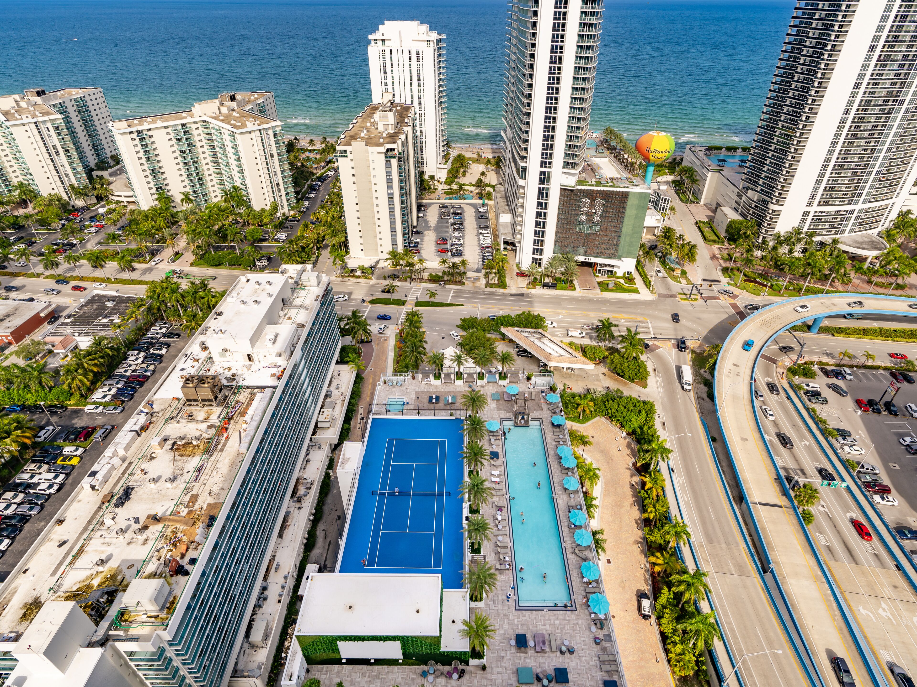 A high-rise hotel with multiple floors, a rooftop pool, and a view of the ocean.