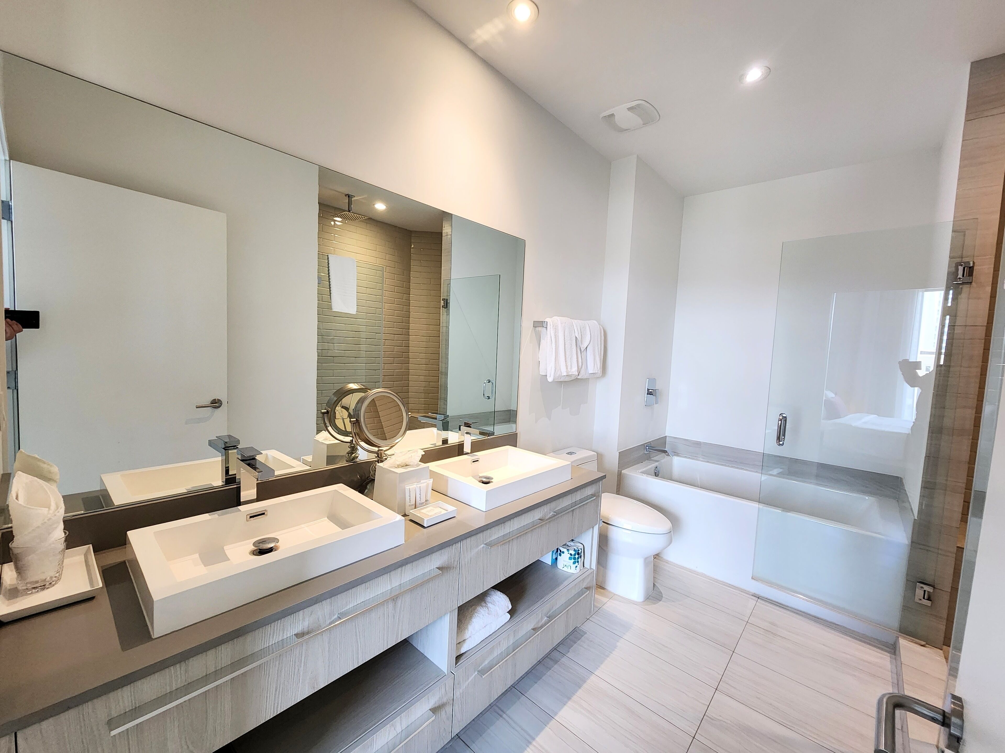 A modern bathroom with two sinks, a large mirror, a glass shower enclosure, and a toilet.