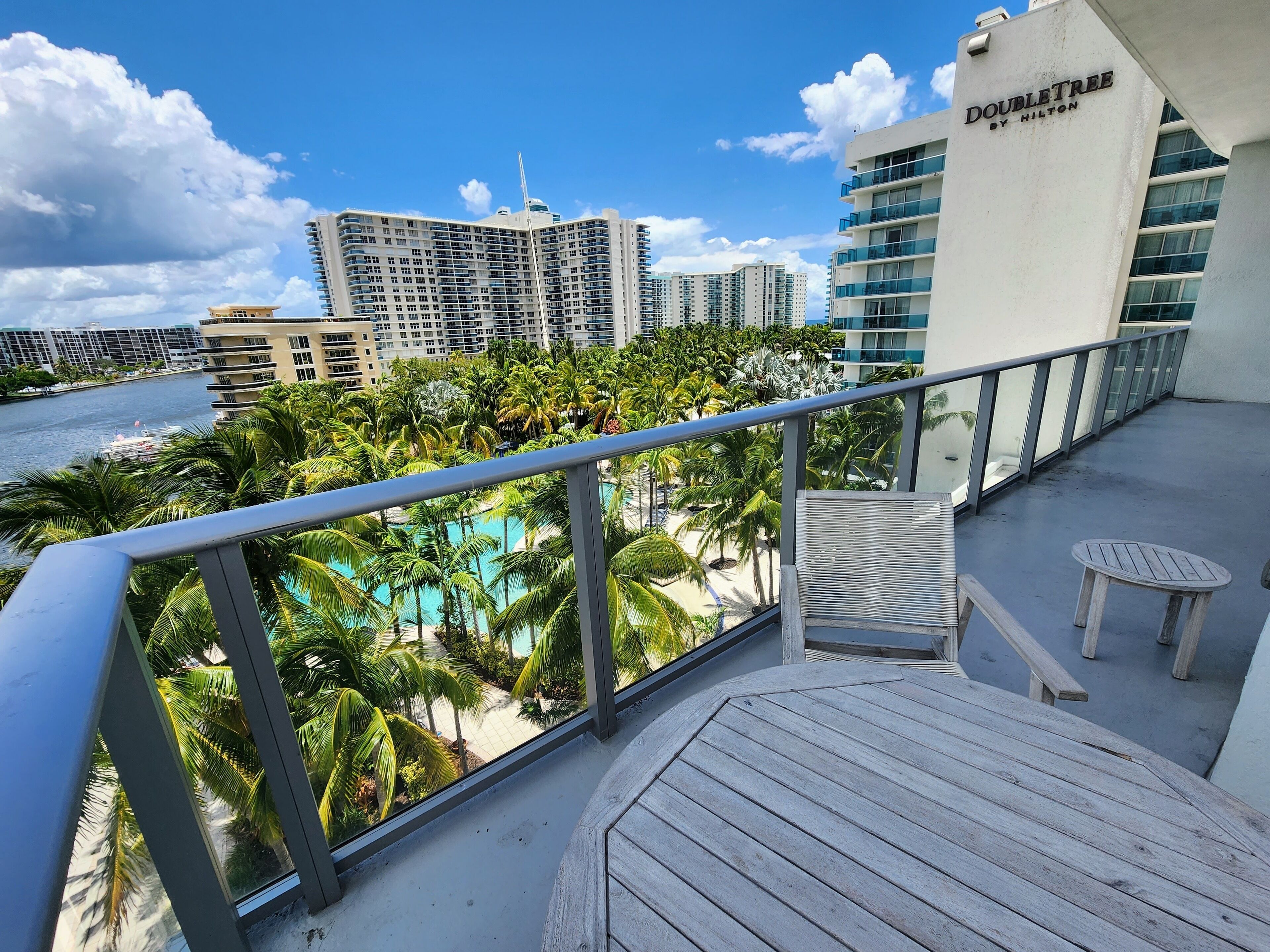 Un balcón con vista a una piscina, palmeras y el horizonte de la ciudad.