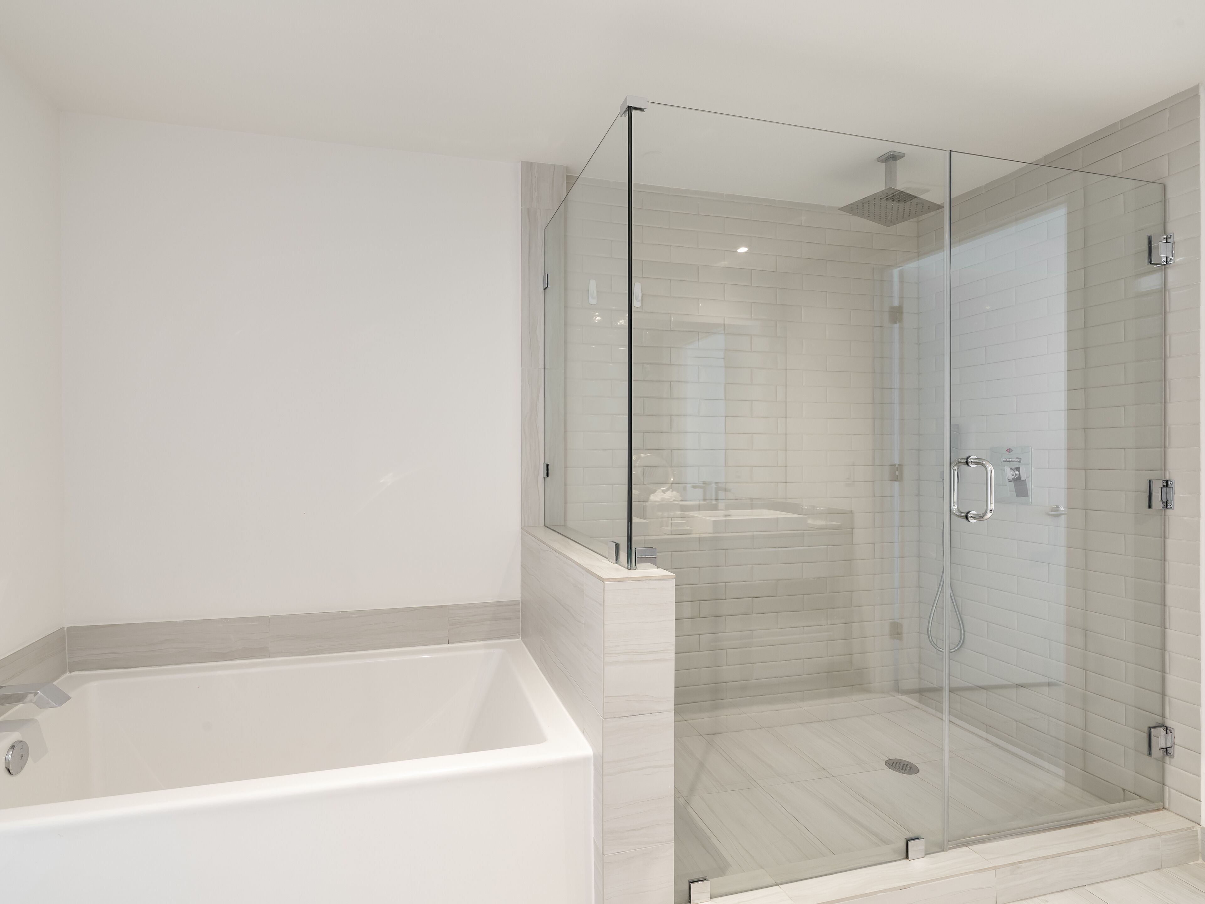 Ein modernes Badezimmer mit einer Glaskabine zur Dusche, einer freistehenden Badewanne und weiß gefliesten Wänden.