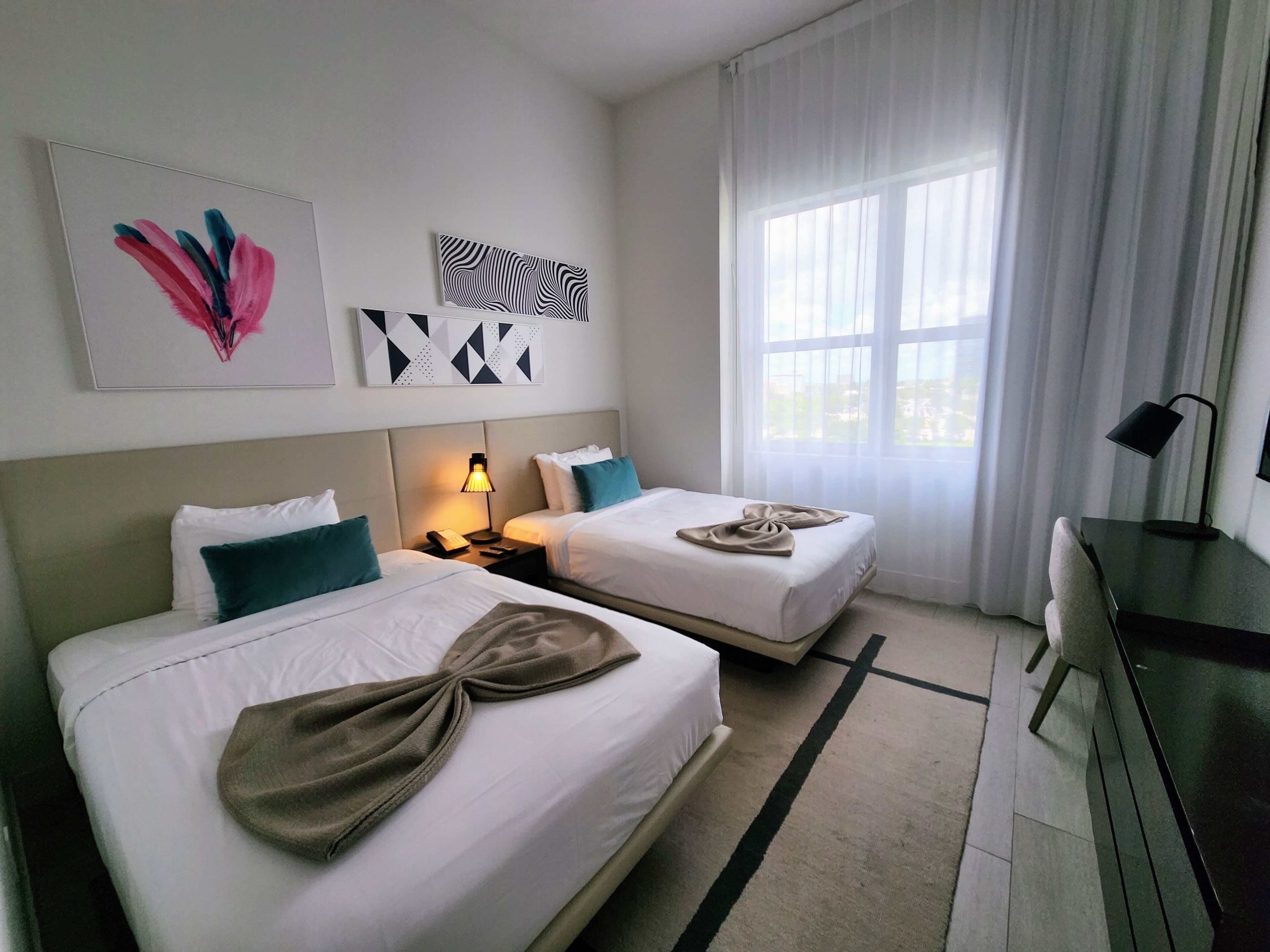 Une chambre d’hôtel avec deux lits, un bureau et une grande fenêtre.