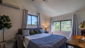 Une chambre à coucher avec un lit, une table de chevet, une lampe et une vue sur les arbres par la fenêtre.